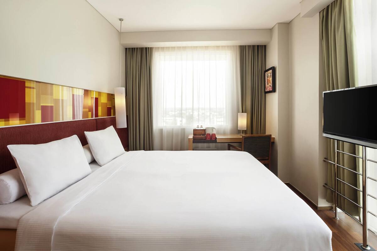 Una habitación de hotel con una cama grande, un escritorio con silla, un televisor y una ventana con cortinas.
