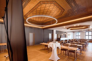 Uma sala de conferências com teto alto, painéis de madeira e um lustre moderno.
