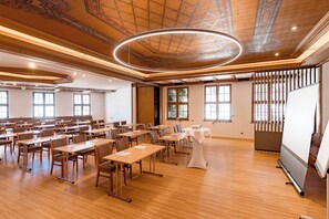 A conference room with multiple tables and chairs, a large circular light fixture, and a projection screen.