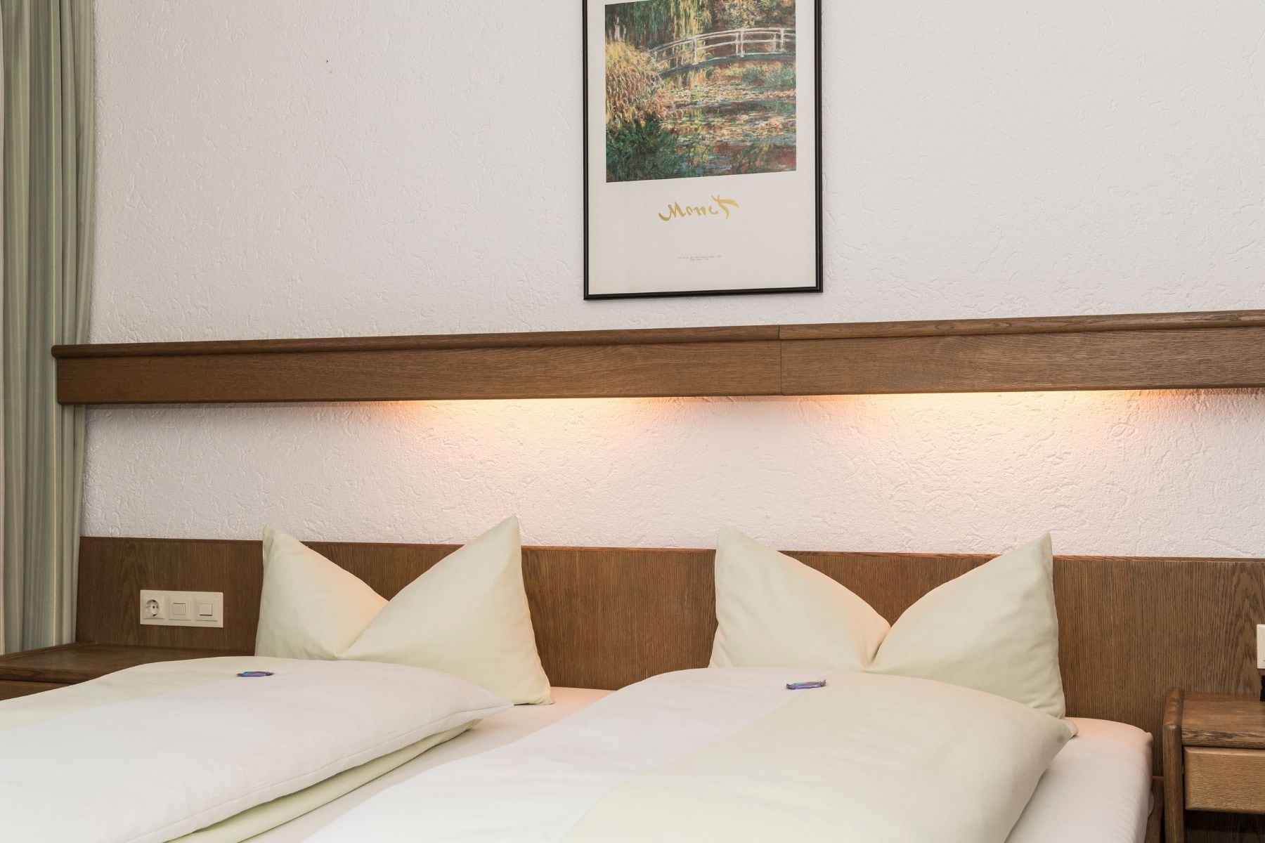 Habitació d'hotel amb un capçal de llit de fusta, un quadre al mur i un llit amb roba de llit blanca.
