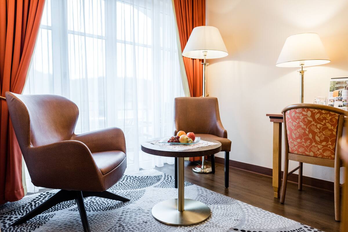 Une chambre d’hôtel avec deux fauteuils, une petite table sur laquelle se trouvent des fruits et deux lampes.