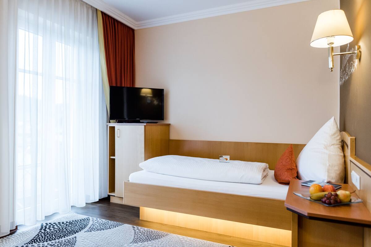 Une chambre d’hôtel avec un lit, une télévision, une table de chevet avec des fruits et une lampe fixée au mur.