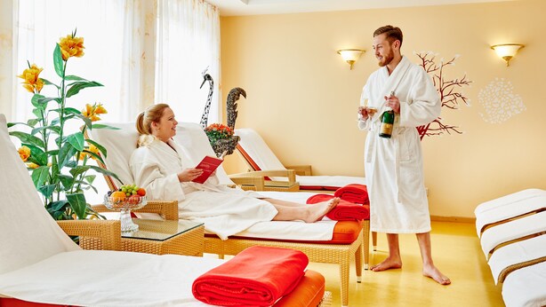 A spa room with two reclining chairs, a large potted plant, and a wall with decorative wall art.