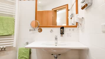 Un baño con un lavamanos blanco, un espejo y un perchero para toallas.