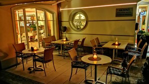 An outdoor seating area with tables and chairs, a round window, and a sign for the Akzent Wellness-Hotel.