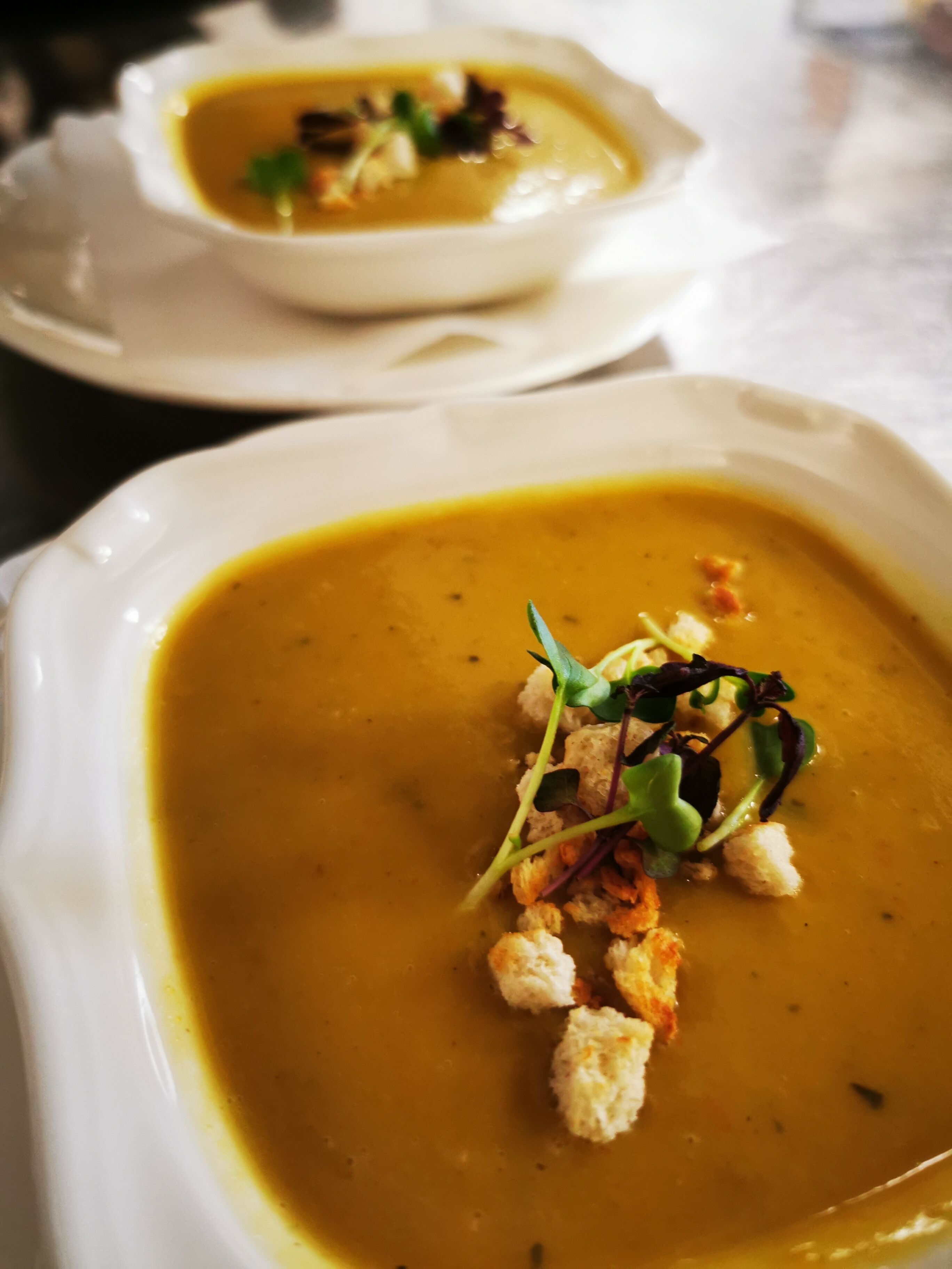 A bowl of soup with croutons and greens on a white plate.