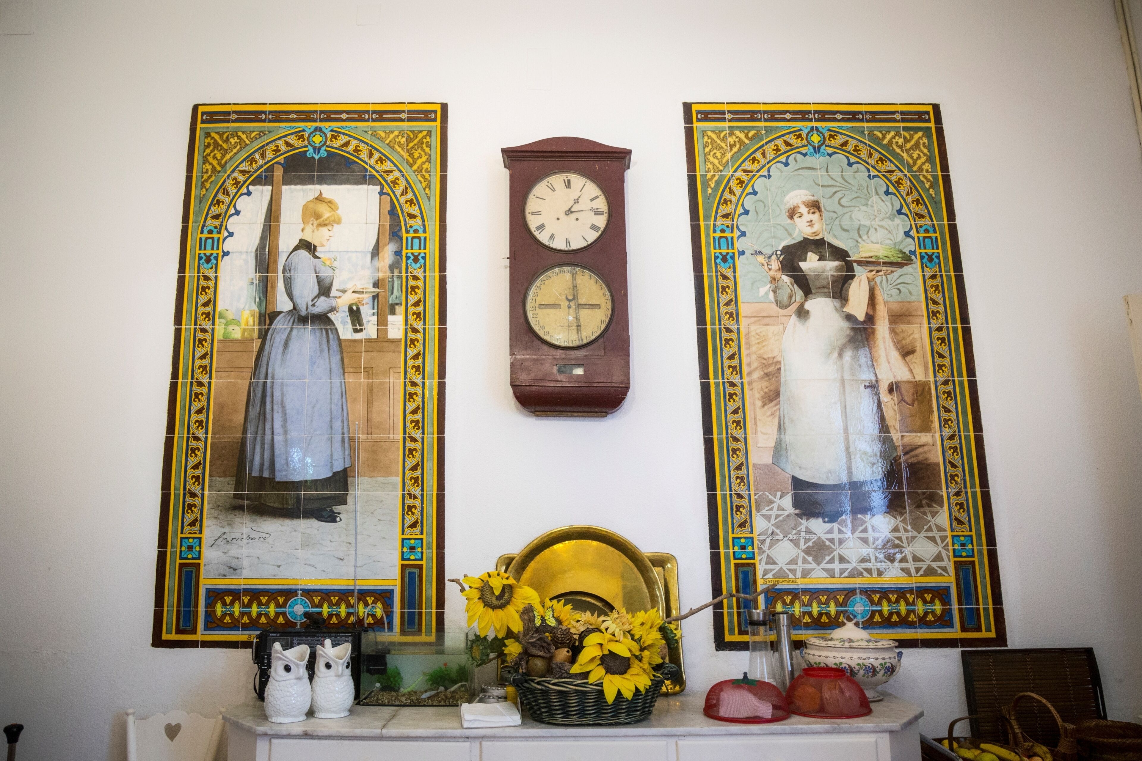 Un mur orné de deux miroirs décoratifs, d’une horloge et d’un panier décoratif contenant des tournesols.