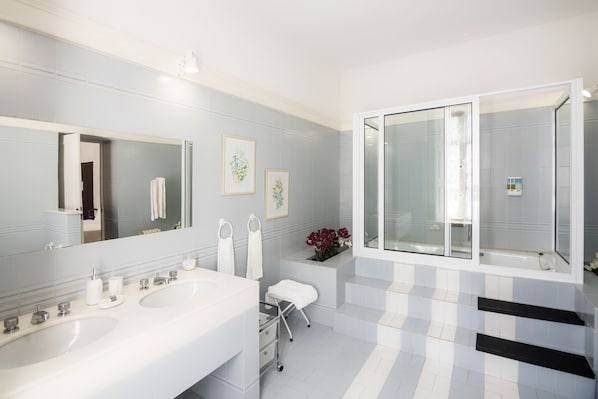 Un baño moderno con dos lavamanos, un espejo grande, una ducha con puerta de vidrio y un pequeño escalón que lleva al inodoro.