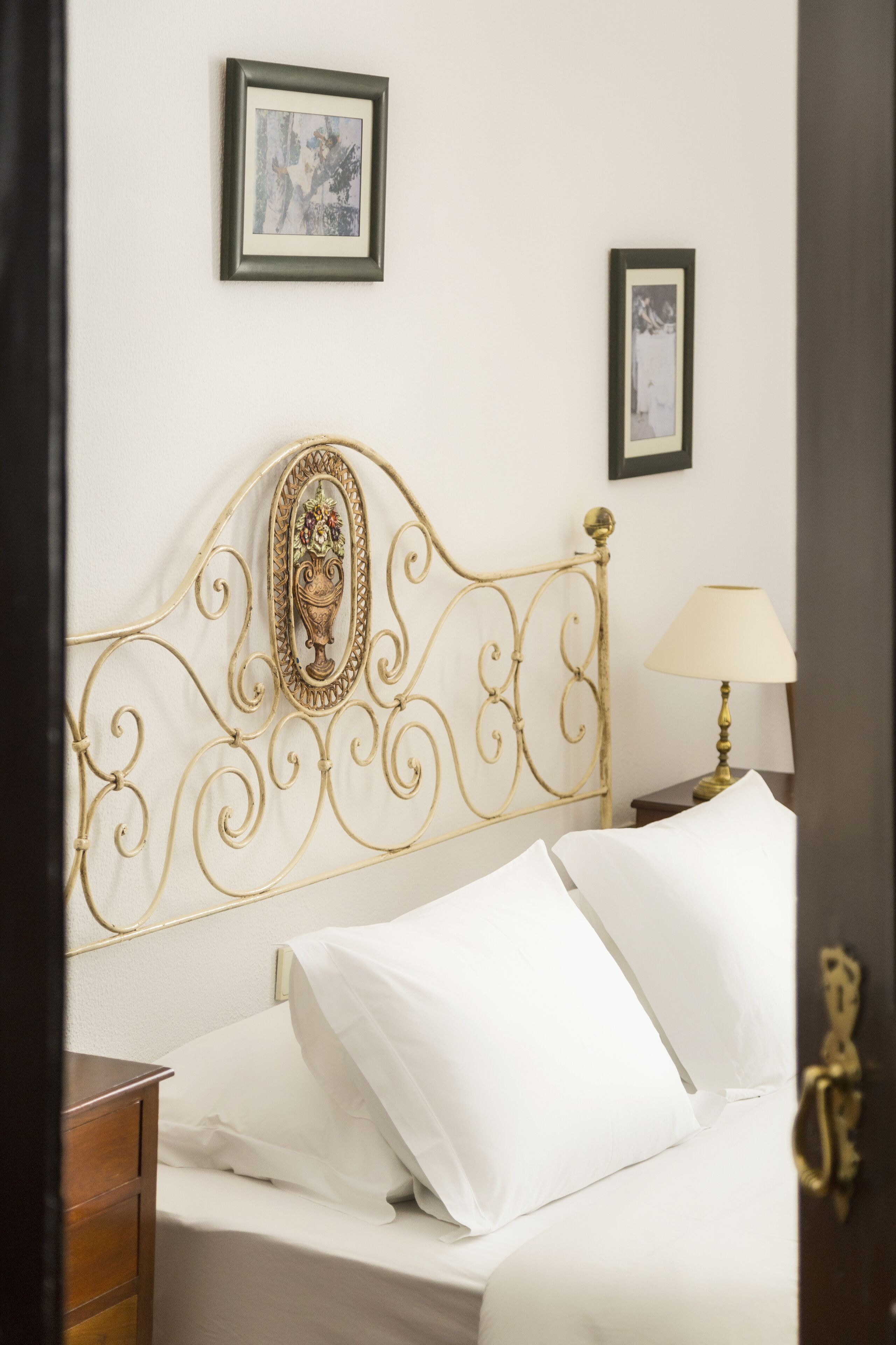 Una cama bien hecha con sábanas blancas, un cabecero decorativo y una mesita de noche con una lámpara.