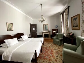 A hotel room with a large bed, a sitting area with a chair, a fireplace, and a mirror on the wall.