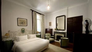 A bedroom with a large bed, a dresser, a chair, a mirror, and a fireplace. - Vila Duparchy (Mealhada)
