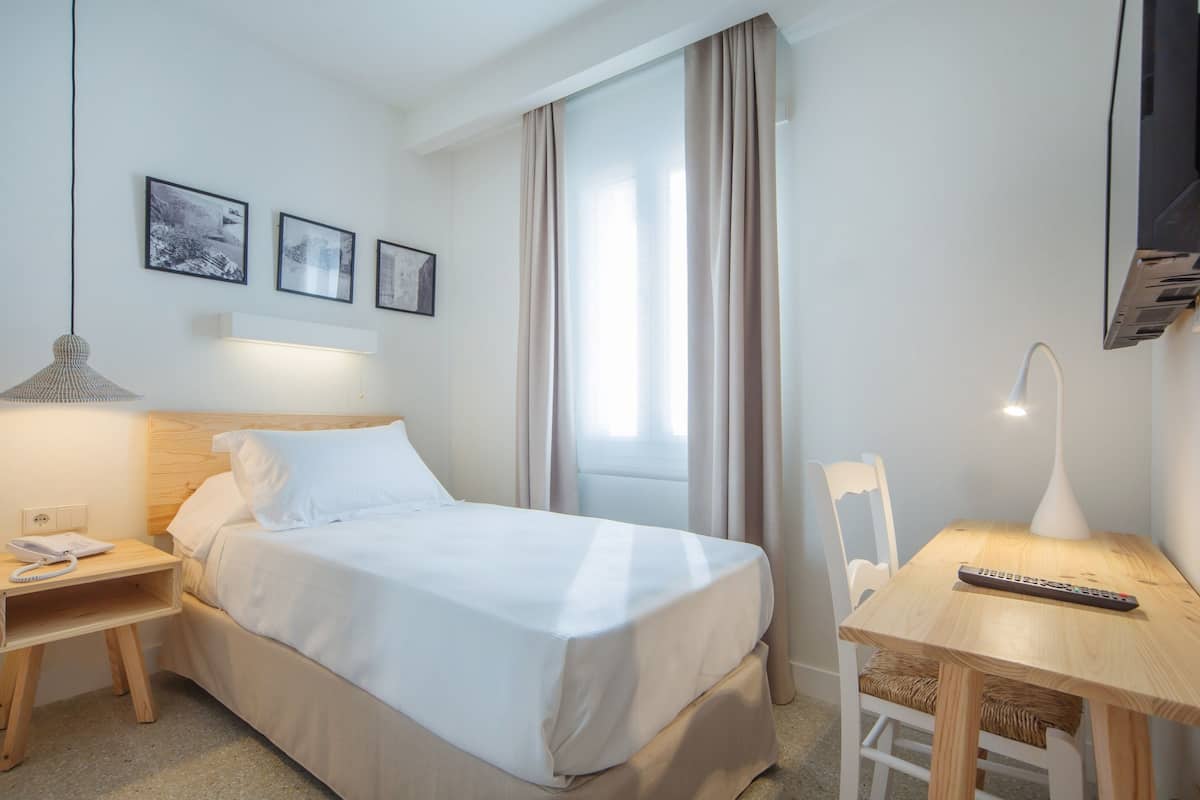 A hotel room with a bed, bedside table, lamp, chair, and a TV.