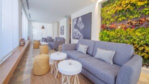 A modern lounge area with a grey sofa, round white tables, and a green wall with plants.