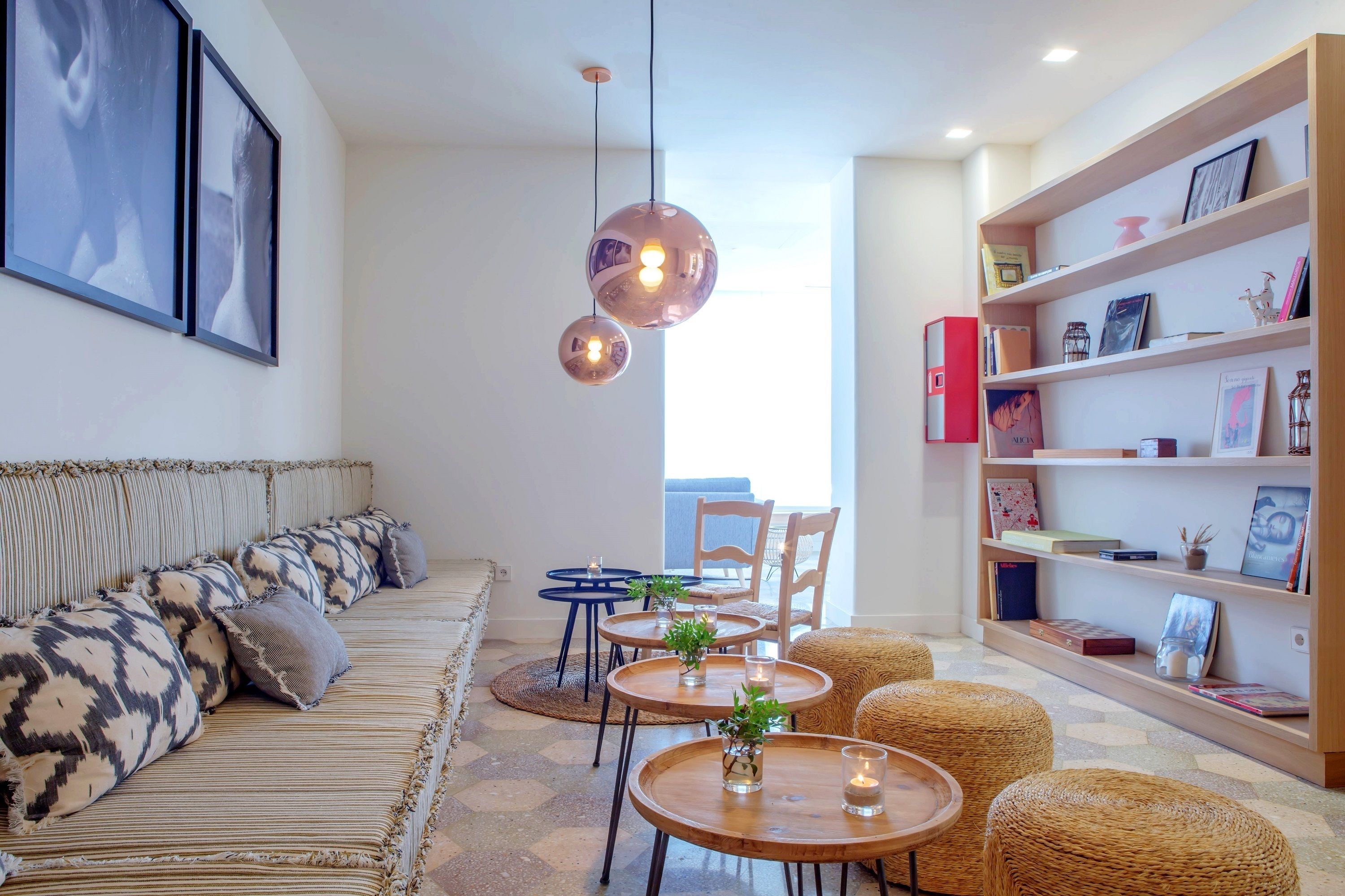Una sala de estar moderna con un sofá, mesas redondas de madera, sillas de mimbre y una estantería.