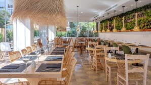 A restaurant with wooden tables and chairs, large windows, and hanging light fixtures.