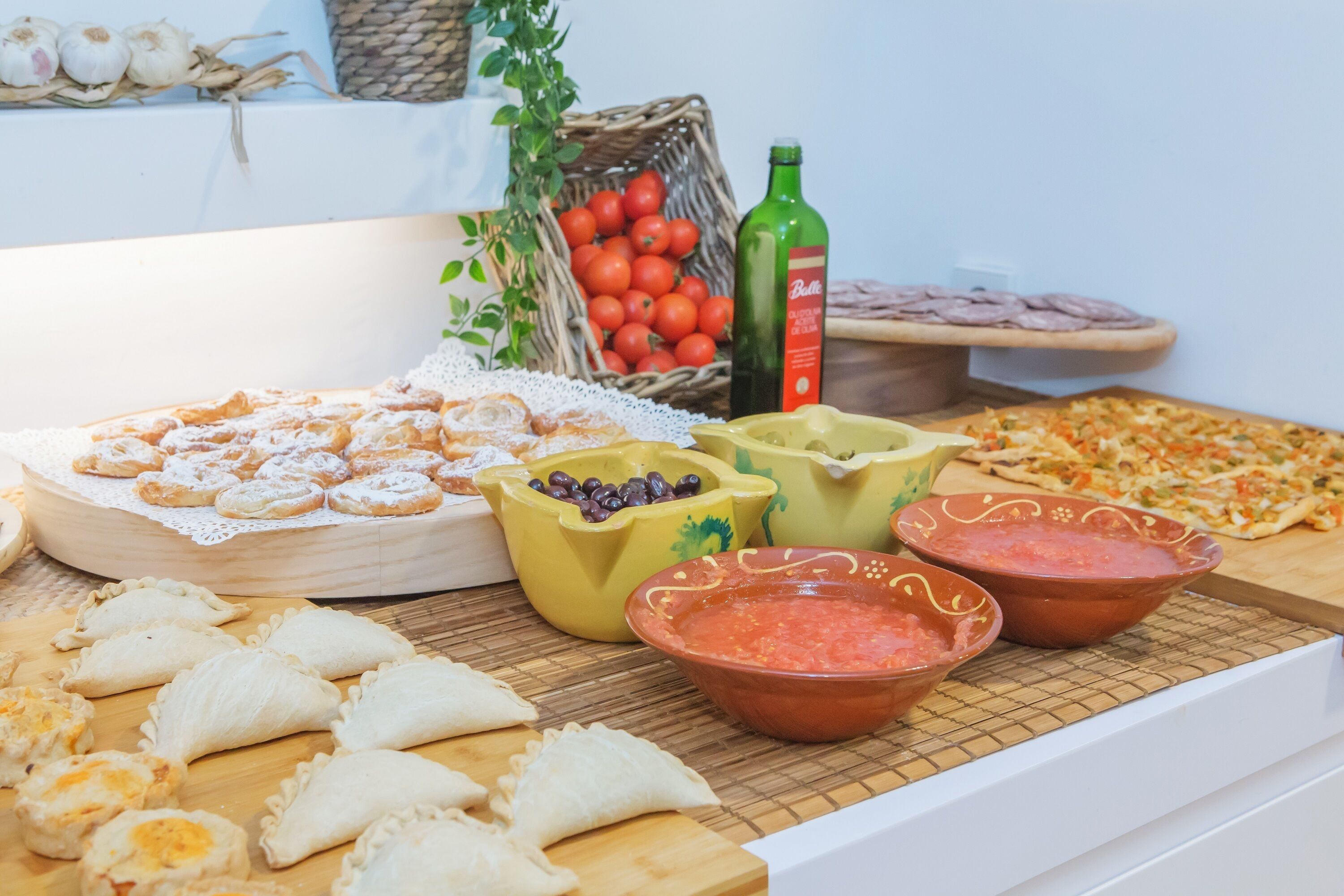 Una mesa de buffet con diversos alimentos, incluyendo pasteles, salsas y una pizza.