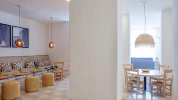 Ein modernes Wohnzimmer mit Sofa, Couchtisch, Hocker und einem Essbereich mit Stühlen und Tisch.
