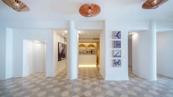 A spacious hallway with a geometric patterned floor, white walls, and a reception area with framed pictures and a small plant.
