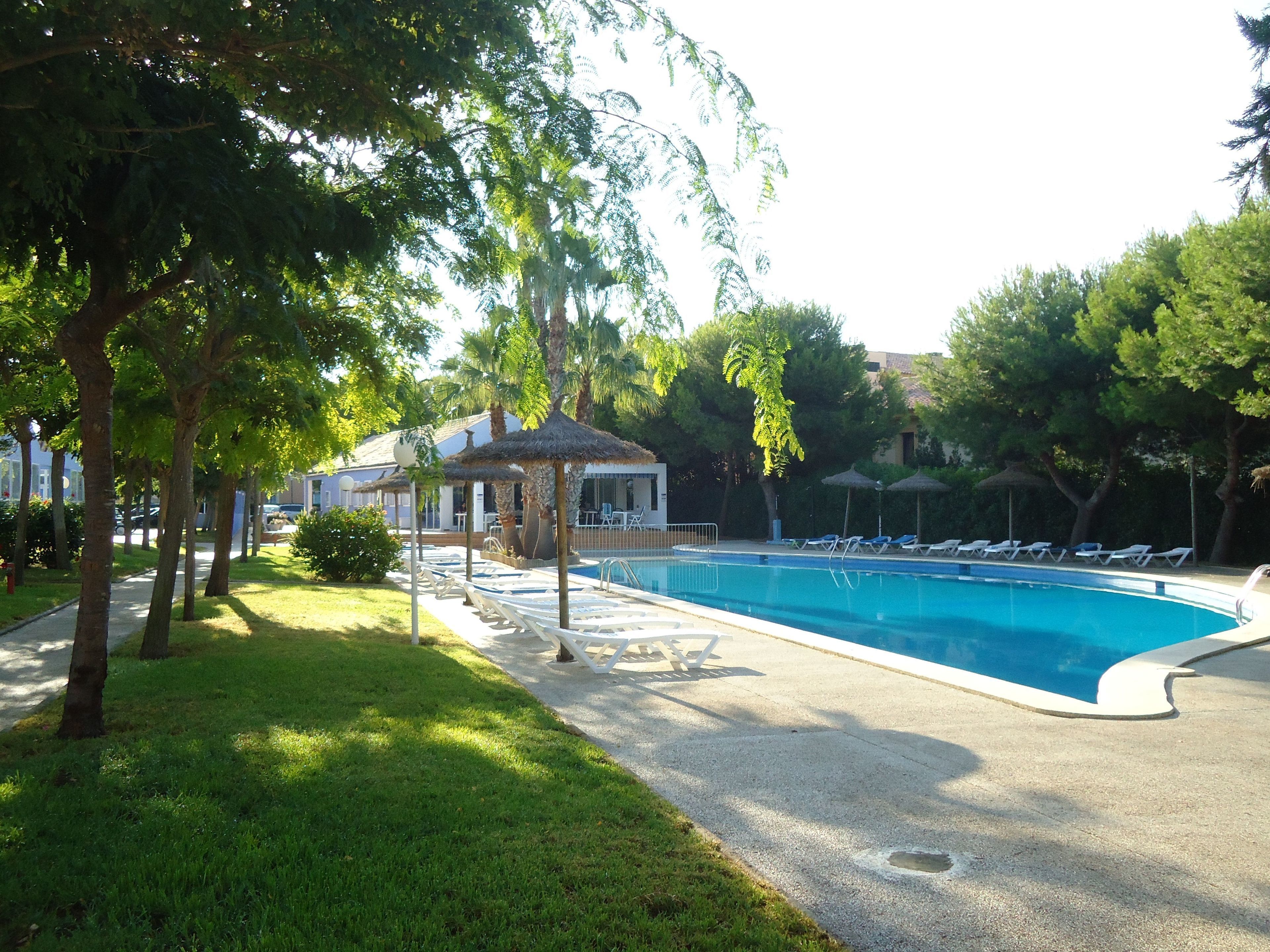 Un área de piscina con sillones de descanso, un pabellón y árboles.