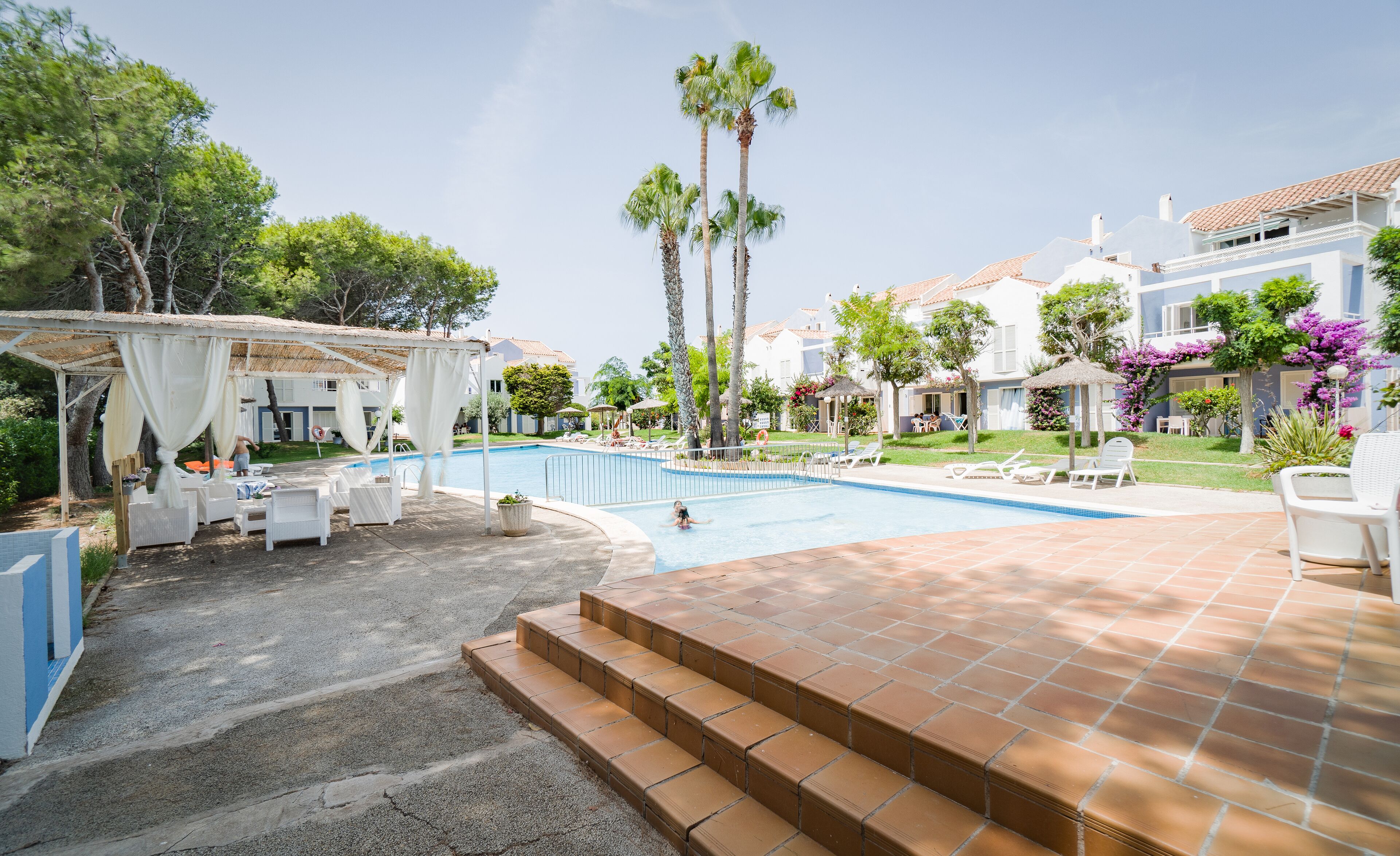 A pool area with lounge chairs and a covered seating area.