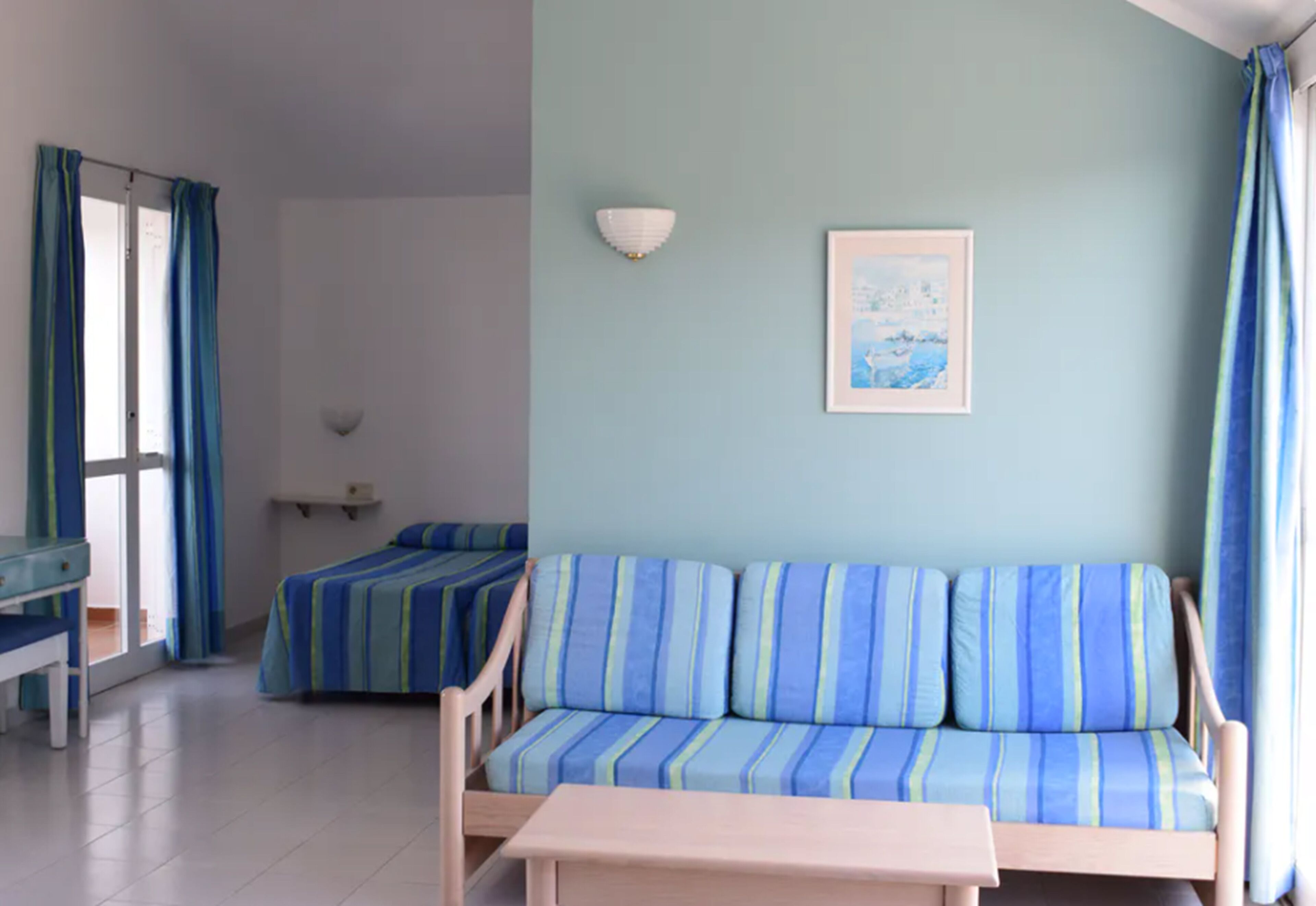 Een kamer met een blauw gestreepte bank, een kleine tafel, een bed en een schilderij aan de muur.