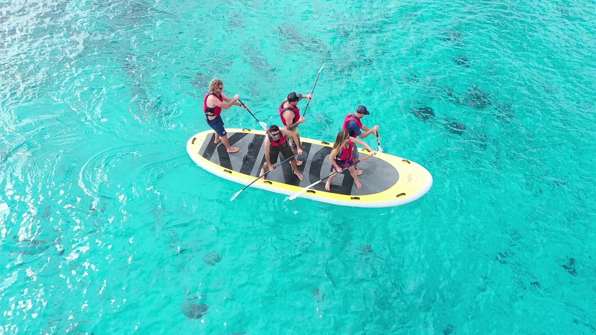 Eine Gruppe von Menschen steht auf Paddleboards in einem klaren, blauen Pool.