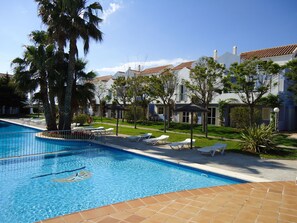 Relax by the clear blue pool surrounded by a tiled deck and lush greenery.