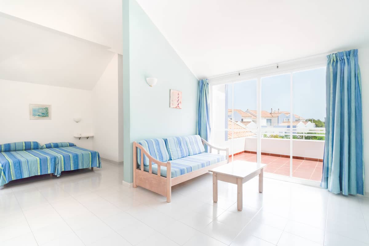 A bright room with a sofa, a small table, and a balcony with a view of buildings.