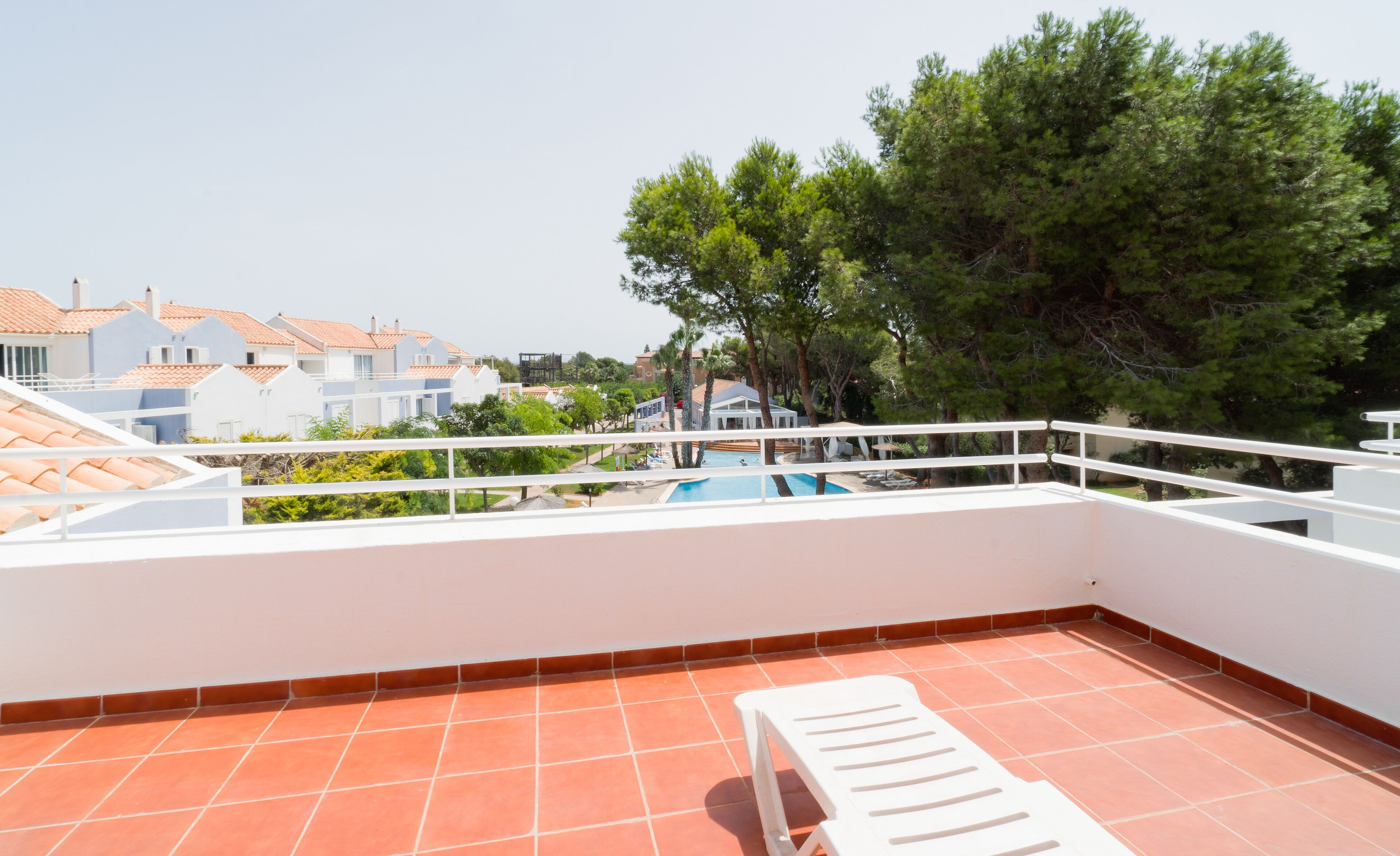 A rooftop terrace with a pool, white railings, and a view of surrounding buildings and trees.