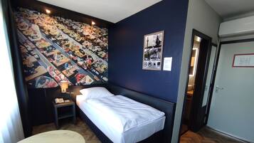 A hotel room with a bed, a round table, a nightstand, a wall mural, and a door.