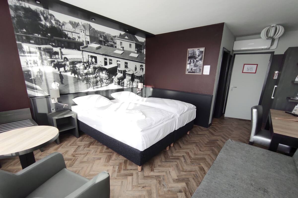 Ein modernes Hotelzimmer mit einem großen Bett, einem Schreibtisch, einem Stuhl und einem Holzboden mit Fischgrätmuster.
