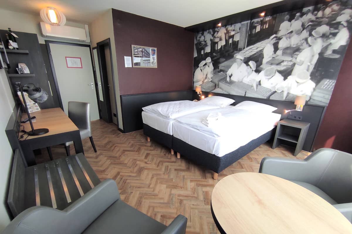 Ein Hotelzimmer mit einem Bett, einem Schreibtisch, einem Stuhl, einem kleinen Tisch und einem großen Wandbild.