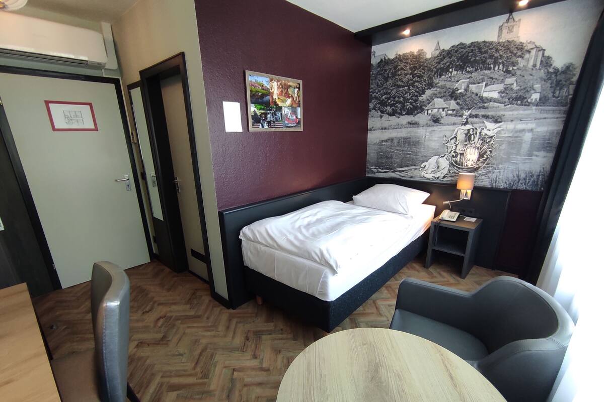 Ein Hotelzimmer mit Bett, Schreibtisch, Stuhl, kleinem Tisch und einer Wand mit Wandgemälde.