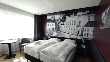 A hotel room with a bed, a round table, and a chair.