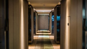 Un couloir au sol décoré de motifs, qui mène à une pièce dont le fond est marqué par une grande porte.