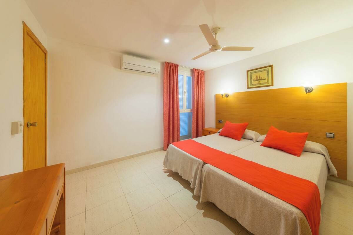 Quarto de hotel com cama, cabeceira de madeira, ventilador de teto e janela com cortinas.