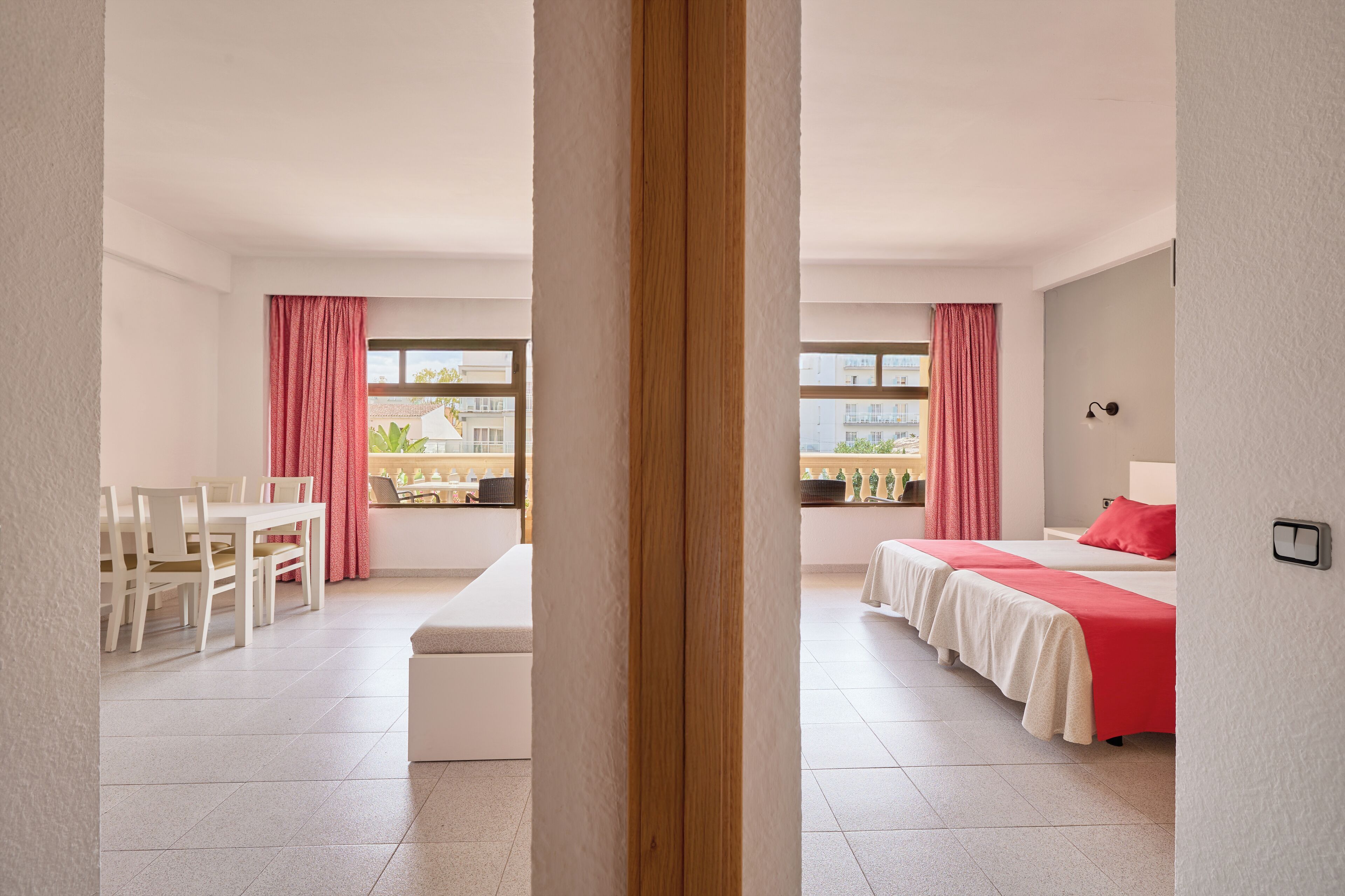 Habitación de hotel con zona de comedor, un ventanal con vistas y una cama con una colcha roja.