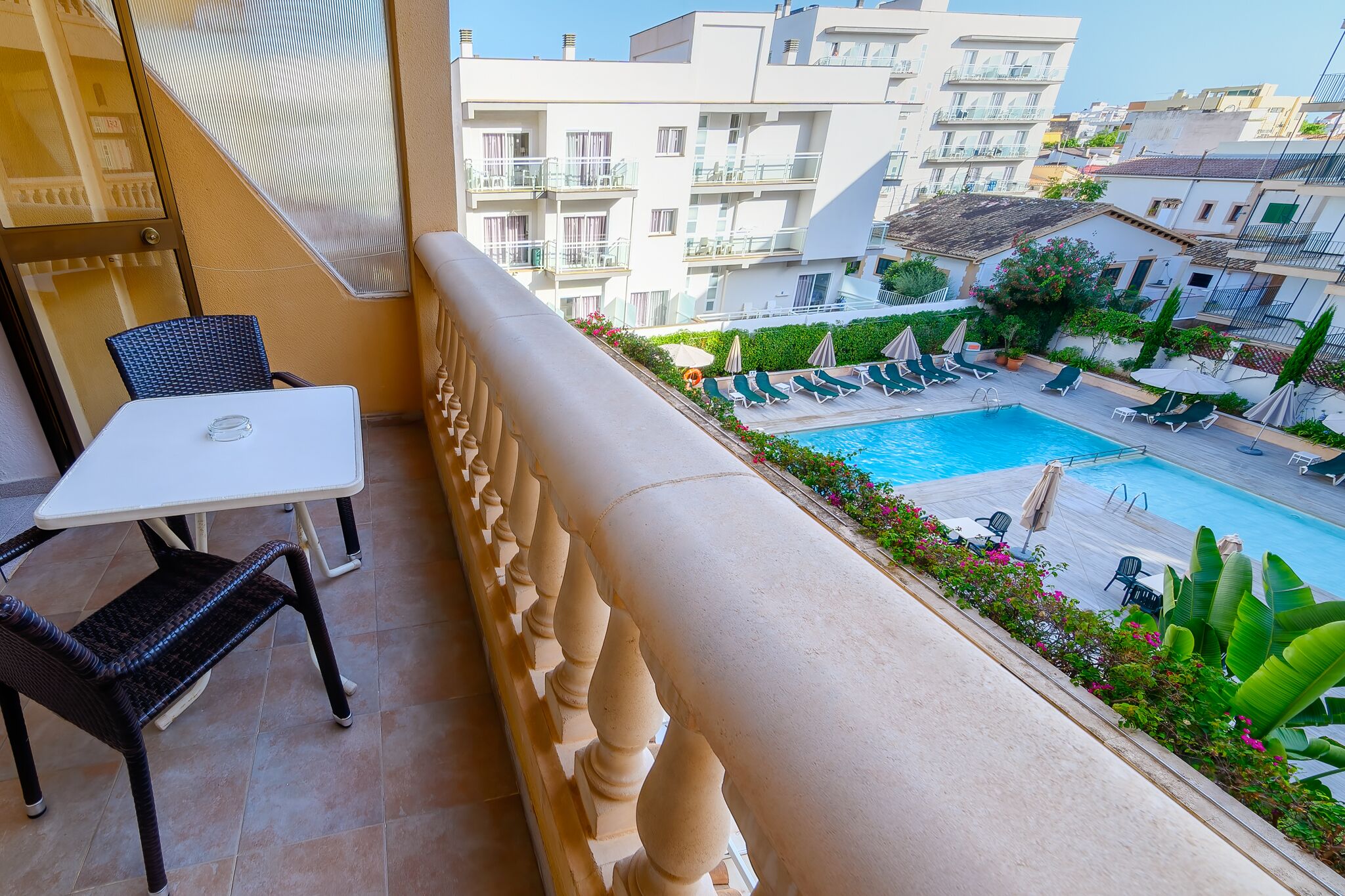 A balcony with a table and chairs, overlooking a swimming pool with lounge chairs and umbrellas.