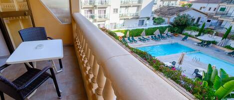 Un balcón con una mesa y sillas, con vista a una piscina con tumbonas y sombrillas.