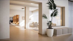 Eine moderne Hotellobby mit einer zentralen Sitzgruppe, einer großen Pflanze und Blick in den angrenzenden Raum.