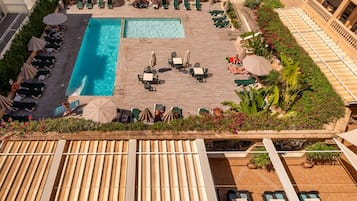 Zona de piscina en la azotea con múltiples sillones de descanso y sombrillas, rodeada de vegetación y plantas en macetas.