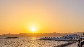 A coastal sunset view with a paved walkway, a pier, and a building with a white facade.