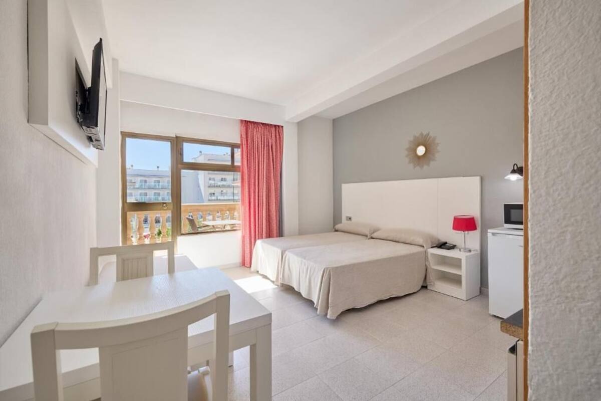 Quarto com cama, escrivaninha e televisão na parede.
