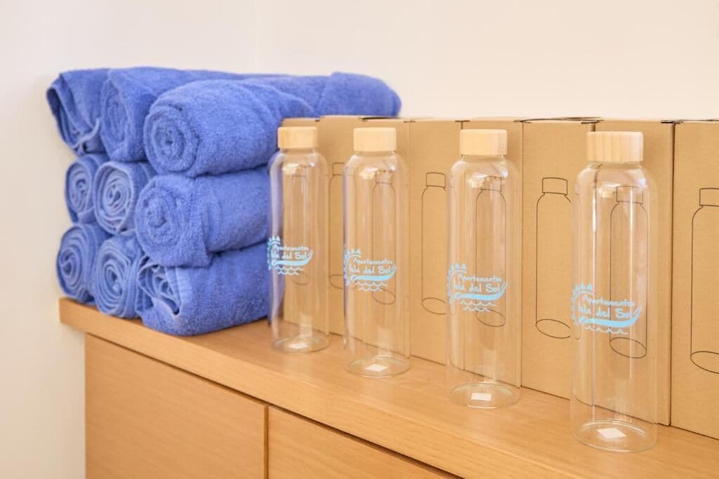 Una encimera de madera con toallas azules enrolladas y botellas de vidrio transparente con un logotipo.