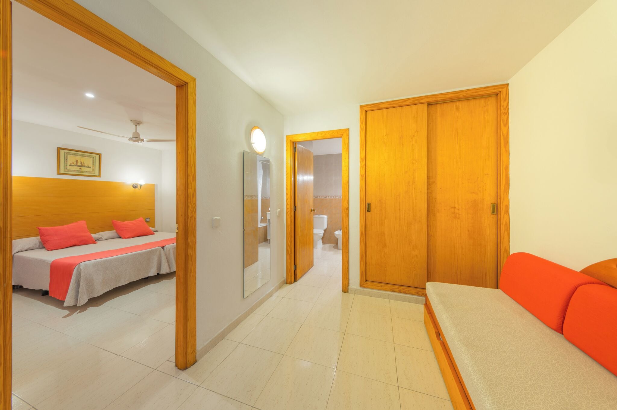 A hotel room with a bed, a sofa, a mirror, and a door leading to a bathroom.