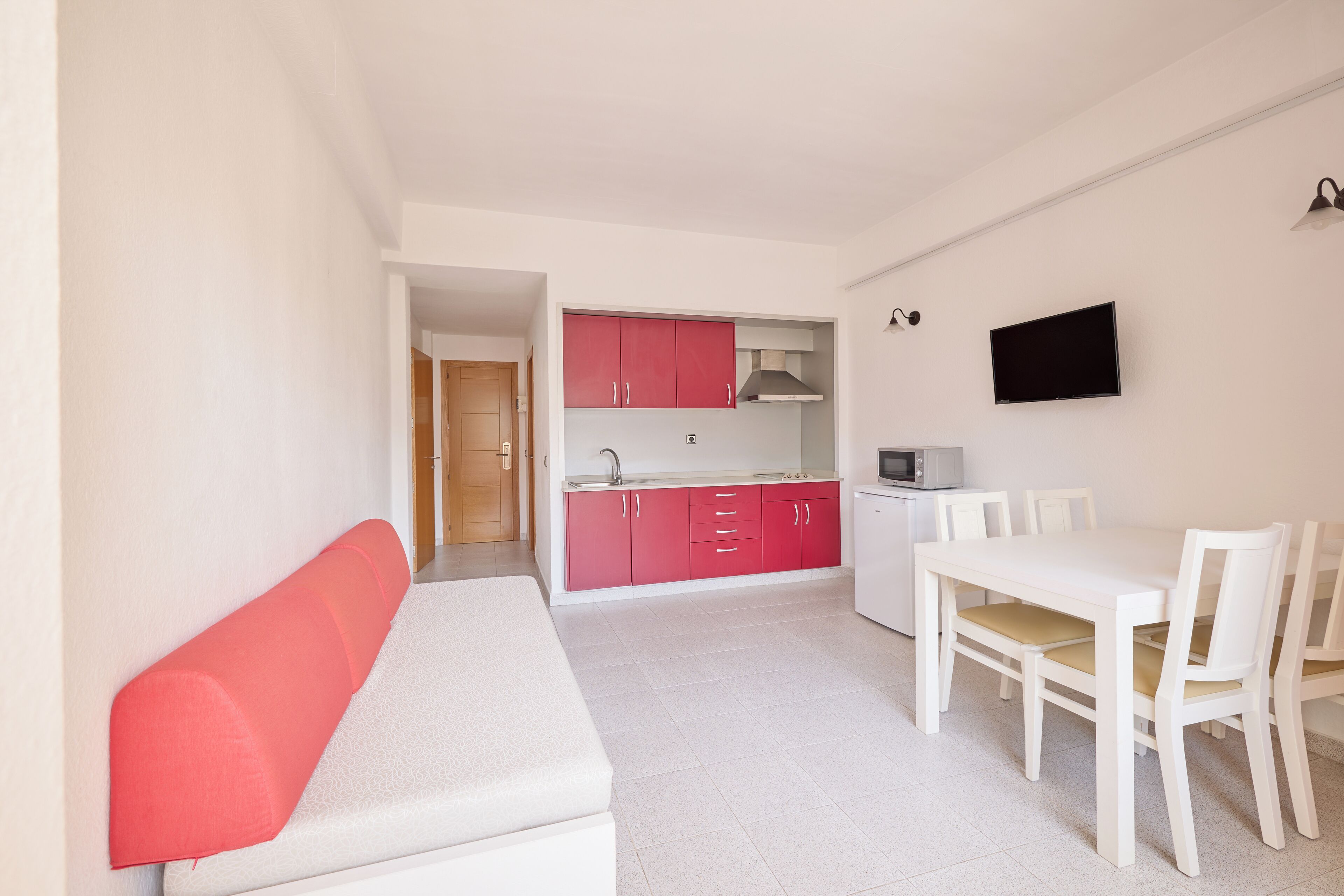 Een kleine keuken met witte en rode kastjes, een magnetron, en een eethoek met een witte tafel en stoelen.
