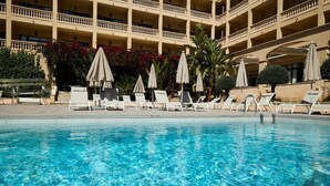 Ein Schwimmbecken mit Liegestühlen und Sonnenschirmen, umgeben von einem mehrstöckigen Gebäude mit Balkonen.