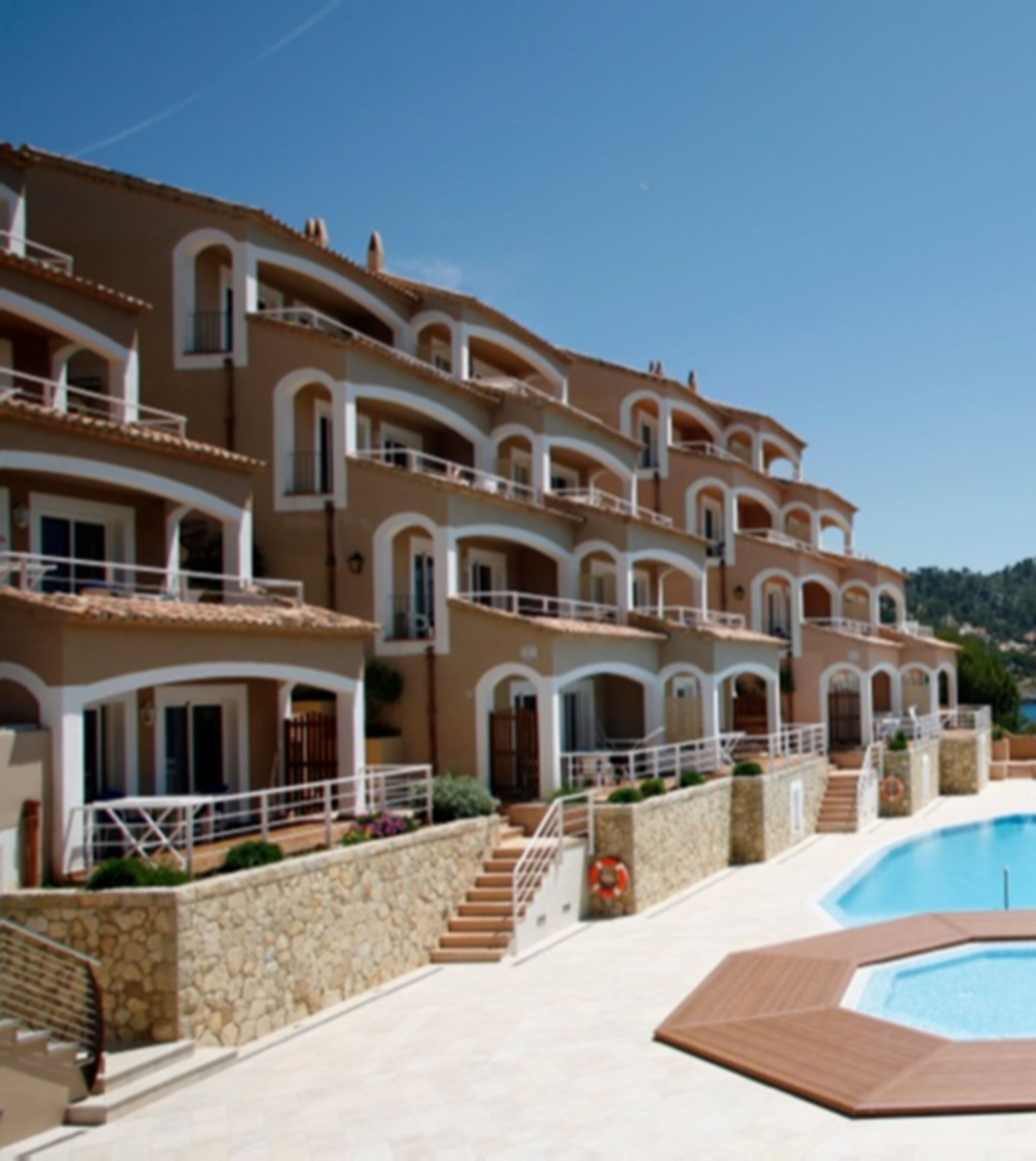 A multi-story hotel with balconies, a swimming pool, and a stone wall.