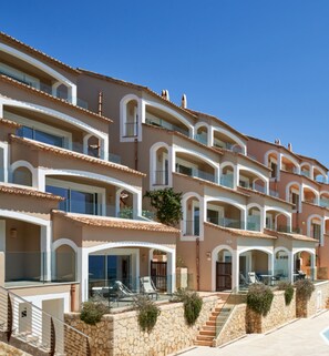Un hôtel à plusieurs étages, doté de balcons et d’une façade en pierre, se dressant sous un ciel d’un bleu limpide.