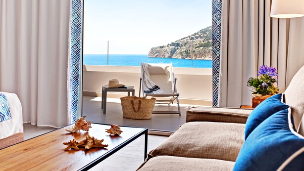 Un balcon avec vue sur la mer, une chaise, une table ornée de coquillages et une lampe.